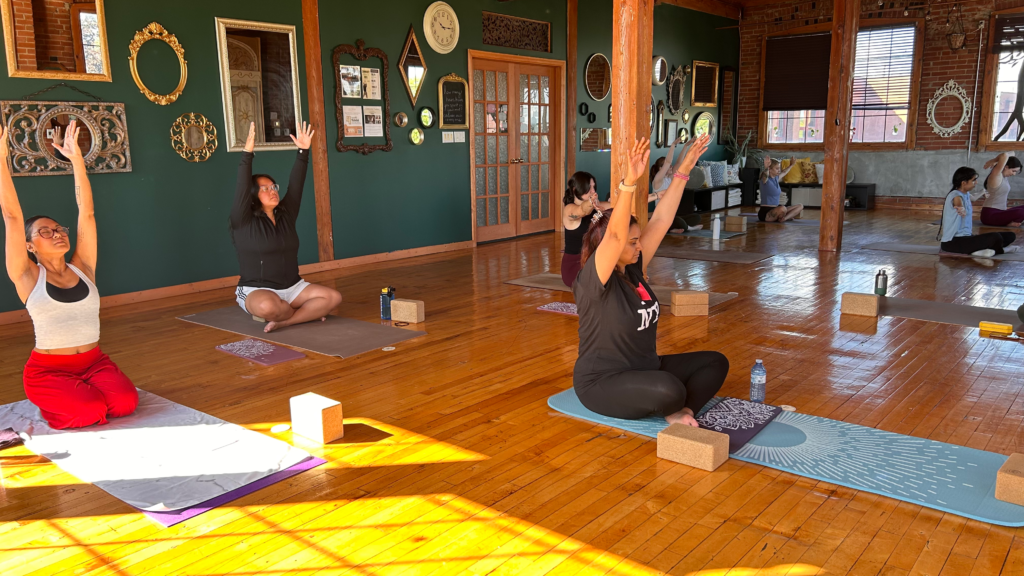 Group of yoga students with arms raised during a class.